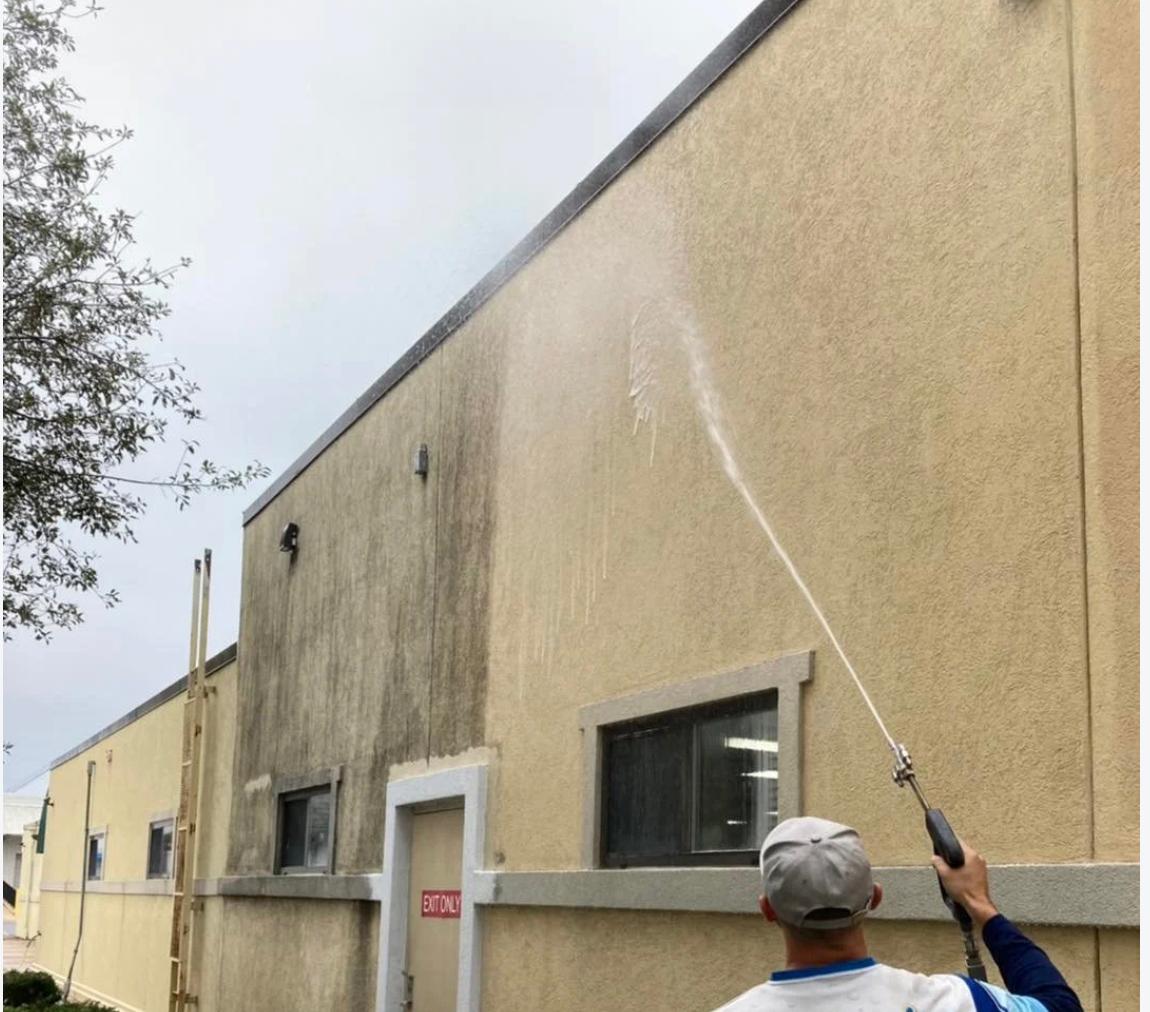 Technician soft washing the exterior wall of a commercial building