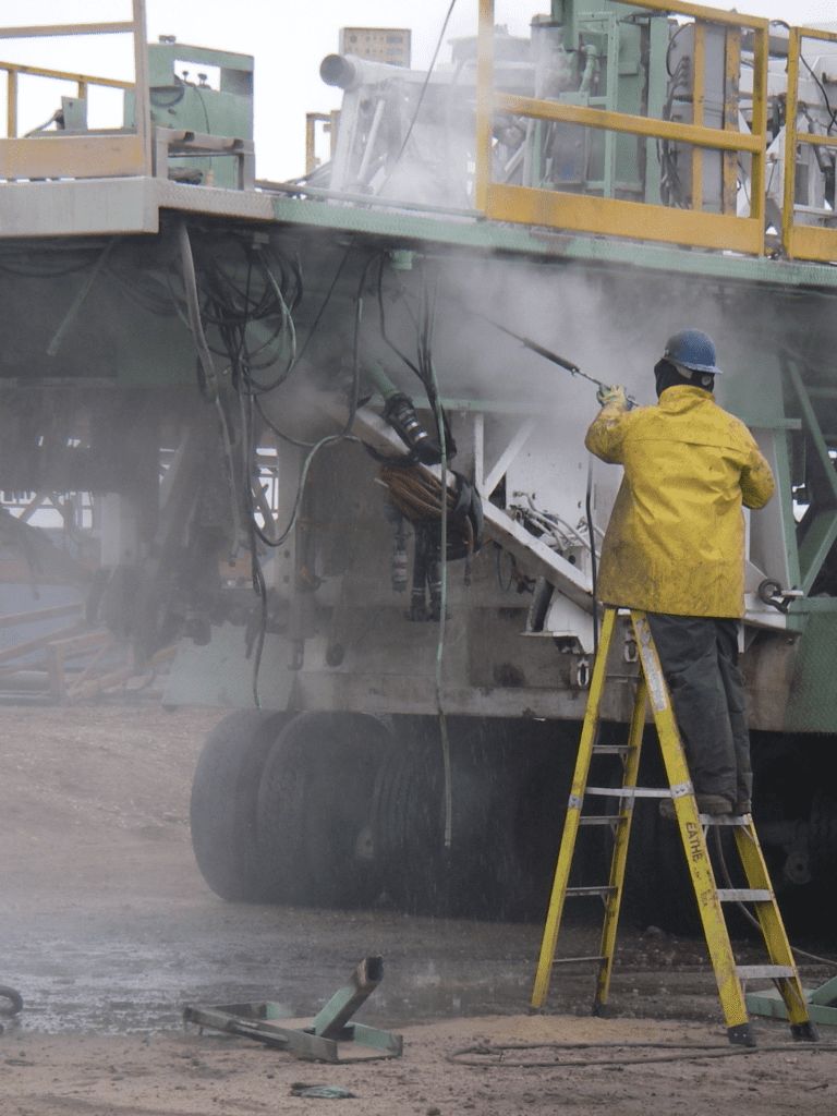 Worker pressure washing a drilling rig